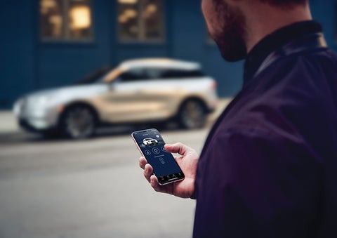 A person is shown interacting with a smartphone to connect to a Lincoln vehicle across the street. | Gettel Lincoln in Punta Gorda FL